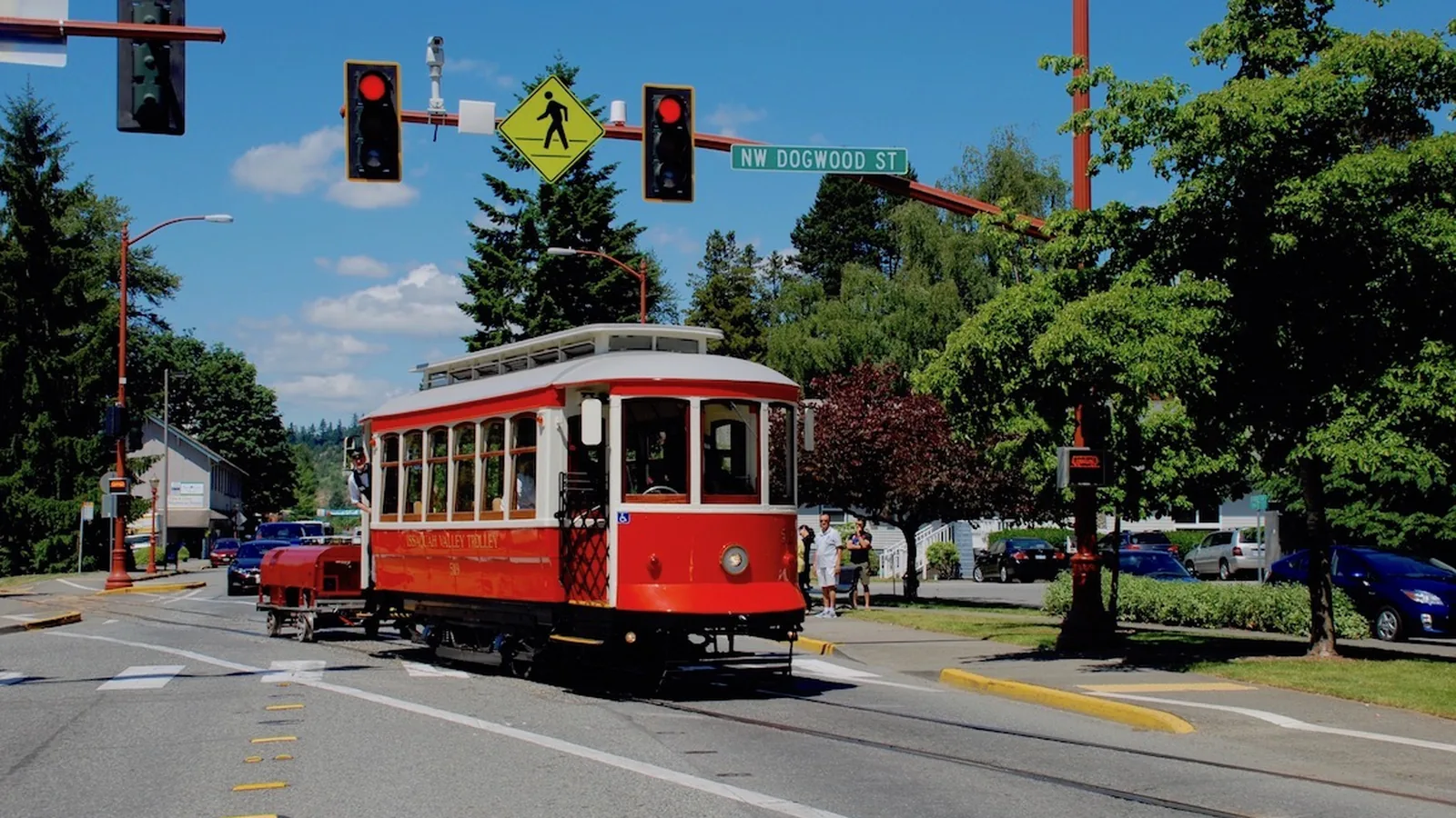 A yellow and green Issaquah Valley Trolley streetcar crossing Front Street, with downtown buildings behind it.