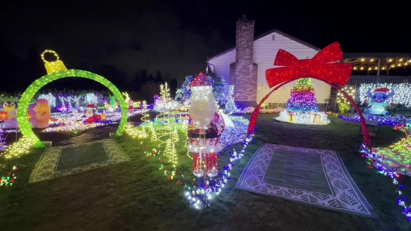 Christmas light tunnels and a train in a front yard at night.